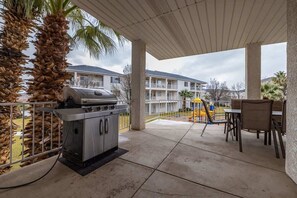An outdoor patio area with a grill, seating, and a view of a residential building. - Las Palmas Resort #1707 | All-Inclusive Amenities (Saint George)