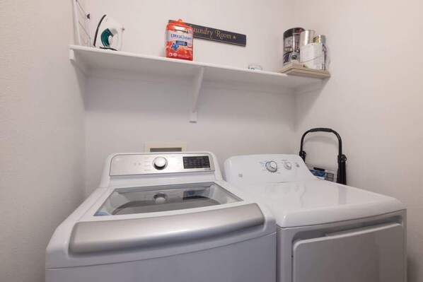 A laundry room with a front-loading washer and dryer, a shelf with laundry supplies, and a wall-mounted laundry sign. - Las Palmas Resort #1707 | All-Inclusive Amenities (Saint George)