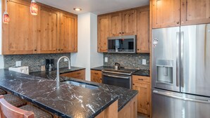 A kitchen with wooden cabinets, a stainless steel refrigerator, a microwave, and a marble countertop. - Classic Ski Condo, Steps to Chair 7 and on shuttle route (Telluride)