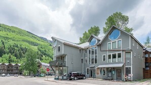 A multi-story building with a balcony, a stop sign, and a parked SUV. - Classic Ski Condo, Steps to Chair 7 and on shuttle route (Telluride)