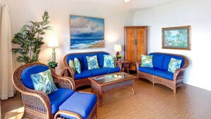 A living room with wicker furniture, a ceiling fan, and artwork on the walls. - Bright, Airy Condo w/Epic View! Wood Floors, Lanai, Full Kitchen, WiFi–Kaha Lani 225 (LIHUE)