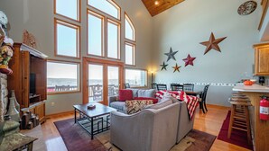 Ein geräumiges Wohnzimmer mit grauem Sofa, einem Holzesstisch und großen Fenstern mit Blick.