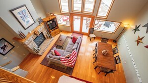 Ein geräumiges Wohnzimmer mit Kamin, einer Couch, einem Esstisch und großen Fenstern.