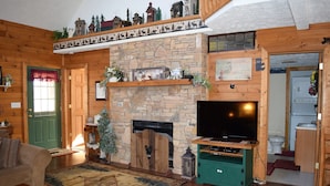 A cozy living room with a stone fireplace, wooden shelves, a television, and a green cabinet.