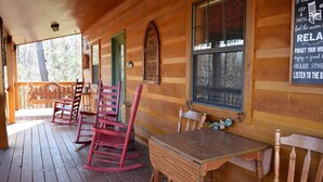 A wooden cabin with a porch, rocking chairs, and a table.