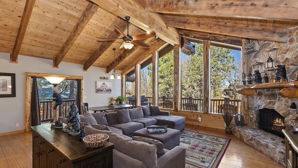 A cozy living room with a sectional sofa, a fireplace, and a stone wall. - Luxury Log Style Home in High Timber Ranch Estates! 1 Block from National Forest! (Big Bear City)
