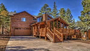 A log cabin with a garage, a covered porch, and a staircase leading to the main entrance. - Luxury Log Style Home in High Timber Ranch Estates! 1 Block from National Forest! (Big Bear City)