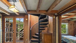 A wooden interior with a spiral staircase, a door leading to a balcony, and a bed with a patterned bedspread. - Unwind on the River, Views, Beaches, Dog Friendly (Forestville)