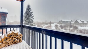 A snowy outdoor area with a wooden deck and a stack of firewood. - Mountainside 2 bedroom. Only minutes from Skiing and hiking trails. (Frisco)