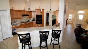 Una cocina amplia con gabinetes de madera, encimera de granito y tres taburetes negros.