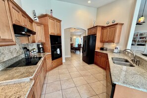 A kitchen with wooden cabinets, a black refrigerator, and a dining area with a chandelier.