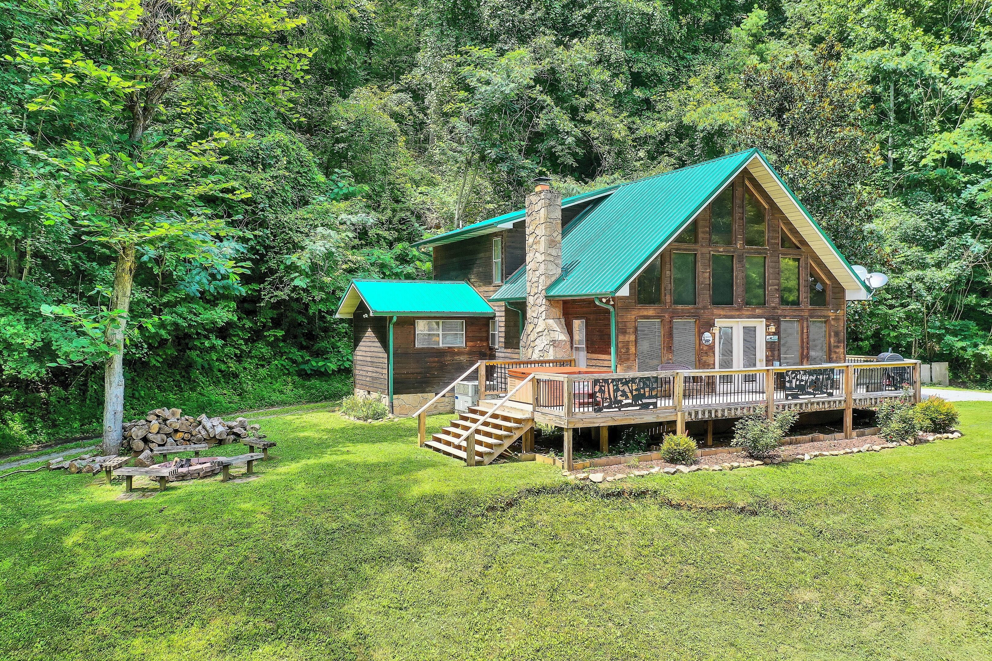 Una cabaña con techo verde, chimenea de piedra y terraza con mobiliario exterior.