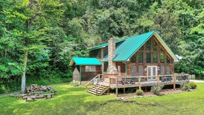 Une cabane dotée d’un toit végétalisé, d’une cheminée en pierre et d’une terrasse avec des sièges d’extérieur.