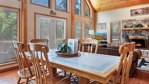 Un intérieur en bois comprenant une table à manger, des chaises, une cheminée et de grandes fenêtres.
