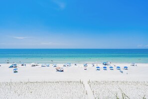 A beach with white sand, clear blue water, and multiple blue umbrellas.