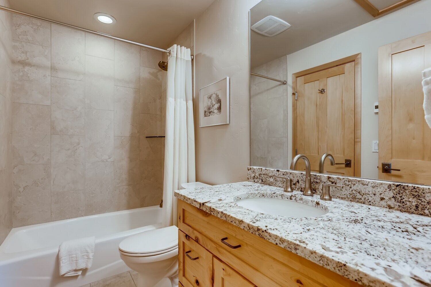 A bathroom with a shower, toilet, and vanity with a sink and mirror.