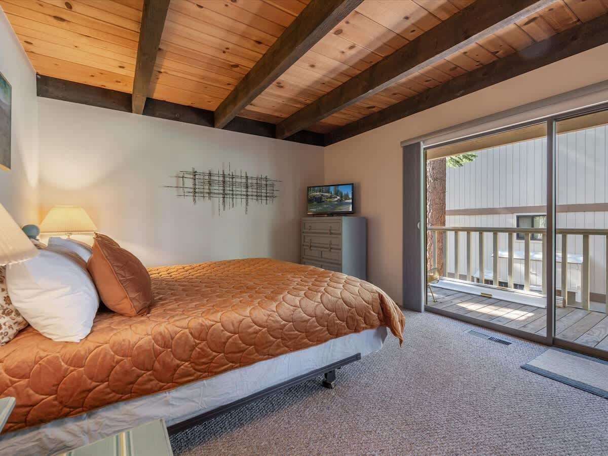 A bedroom with a bed, a TV, a wooden ceiling, and a sliding glass door leading to an outdoor area.