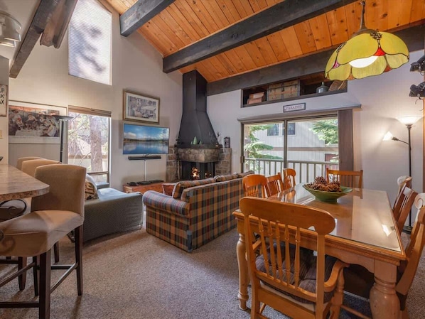 A cozy living room with a fireplace, plaid sofa, wooden dining table, and chairs.