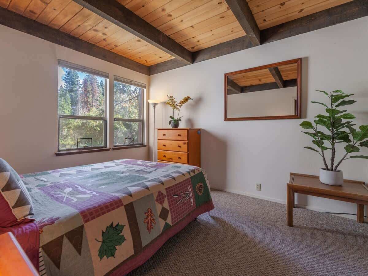 A bedroom with a bed, dresser, mirror, and potted plant.