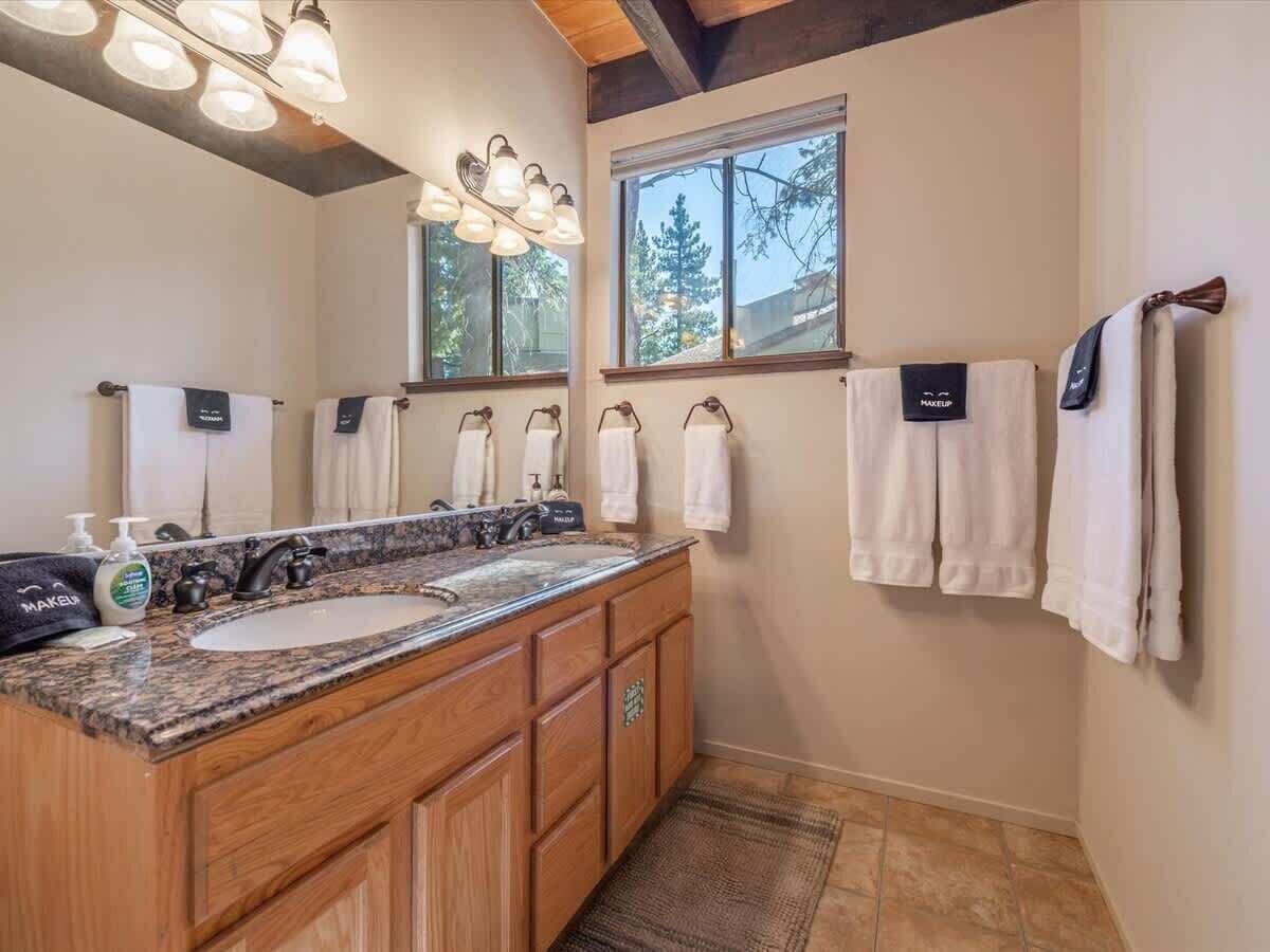 A bathroom with a granite countertop sink, wooden cabinets, a large mirror, and multiple towels hanging on a rack.