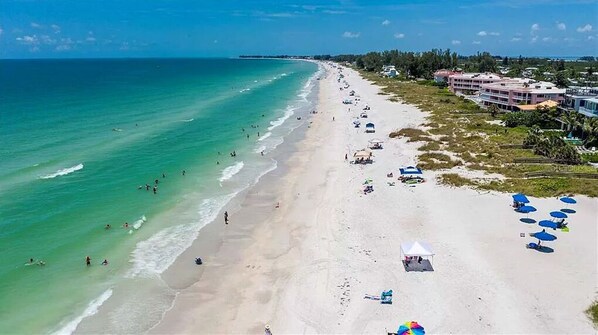 A beach with a row of beach umbrellas and a white tent on the sand.