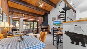 Un intérieur chaleureux avec une table à carreaux, des meubles en bois, une cheminée, un téléviseur et un ours en guise de décoration.