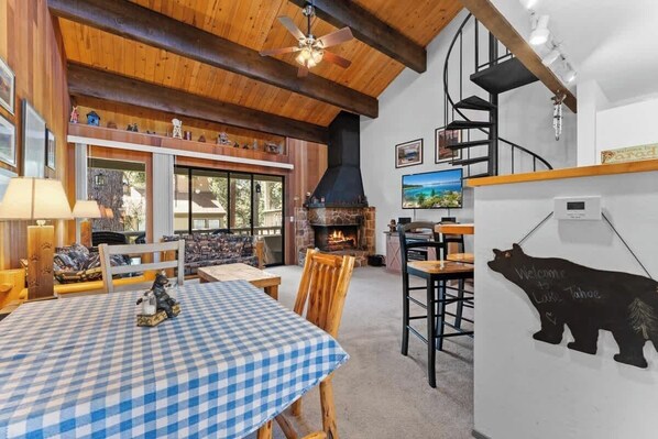 A cozy interior with a checkered table, wooden furniture, a fireplace, a TV, and a bear decoration.