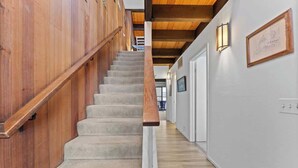 Un escalier en bois menant à un palier avec un mur blanc et des œuvres d’art encadrées.