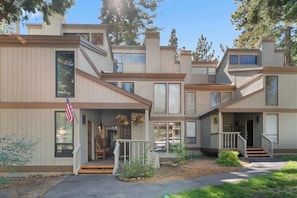 A multi-story residential building with a front porch, a flag, and a small garden area.