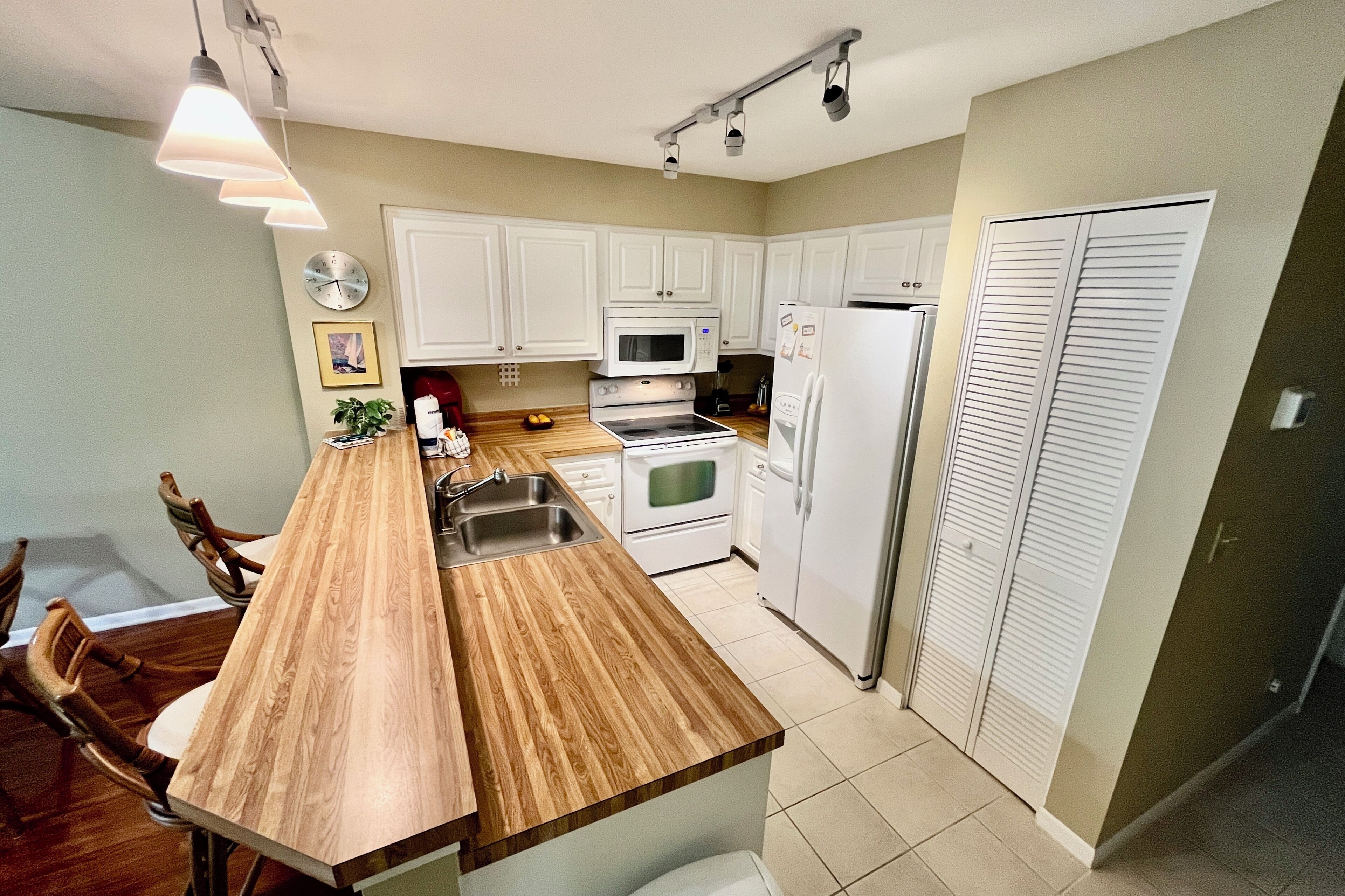 A kitchen with white cabinets, a wooden island with a sink, a microwave, an oven, and a refrigerator.