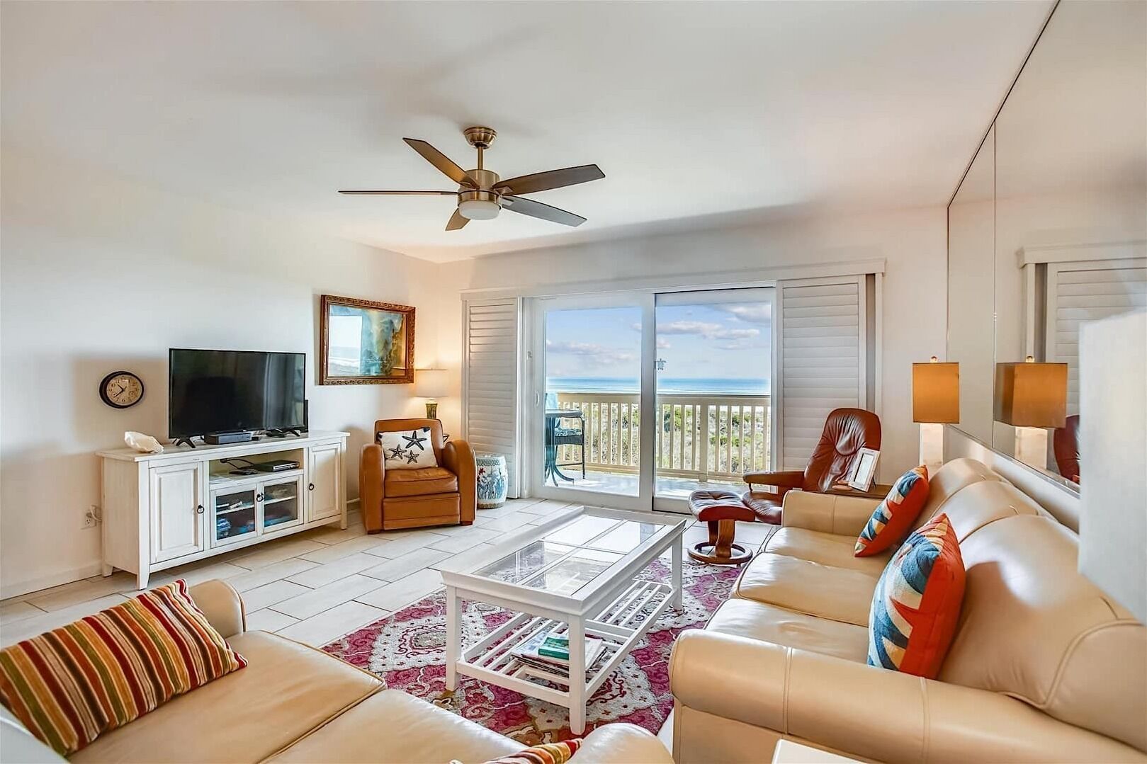 A spacious living room with a flat-screen TV, leather sofas, a coffee table, and a ceiling fan.