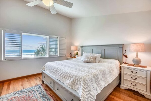 A bedroom with a bed, a nightstand, a lamp, and a view of the ocean through the window.