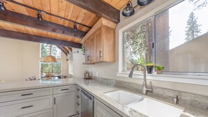 Une cuisine avec des meubles de rangement en bois, une grande fenêtre et un lave-vaisselle encastré.