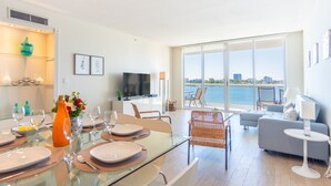 Un salon moderne avec un coin repas, de grandes fenêtres et une vue sur l’eau.