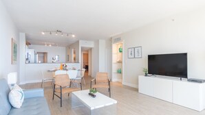 Un salon moderne avec un canapé, des fauteuils, une table basse et un téléviseur posé sur un meuble blanc.