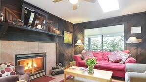 A cozy living room with a fireplace, a red sofa, and a wooden ceiling. - Boathouse ~ On River, Deck, Steps to Beach, Family  Dog Friendly! (Guerneville)