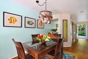 Un comedor con una mesa de vidrio, sillas de madera, una lámpara colgante decorativa, cuadros de peces enmarcados y un letrero de bienvenida.
