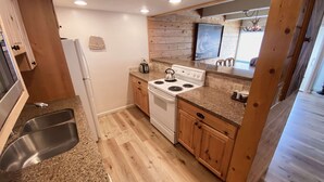 A compact kitchen with a stove, sink, and wooden cabinets. - Vail Mountain Views from Balcony, Outdoor Hot Tub & Pool, Free Parking - Walk to Lionshead (Vail)