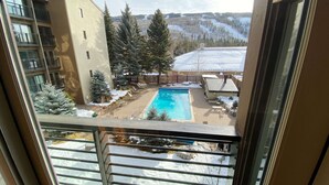 A view of a swimming pool surrounded by snow-covered ground and trees, with a building in the background. - Vail Mountain Views from Balcony, Outdoor Hot Tub & Pool, Free Parking - Walk to Lionshead (Vail)