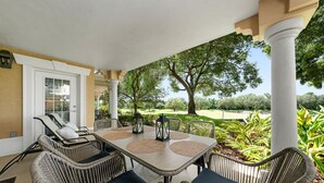Une terrasse couverte, meublée de meubles en osier, avec une table agrémentée de sets de table, et offrant une vue sur un terrain de golf.
