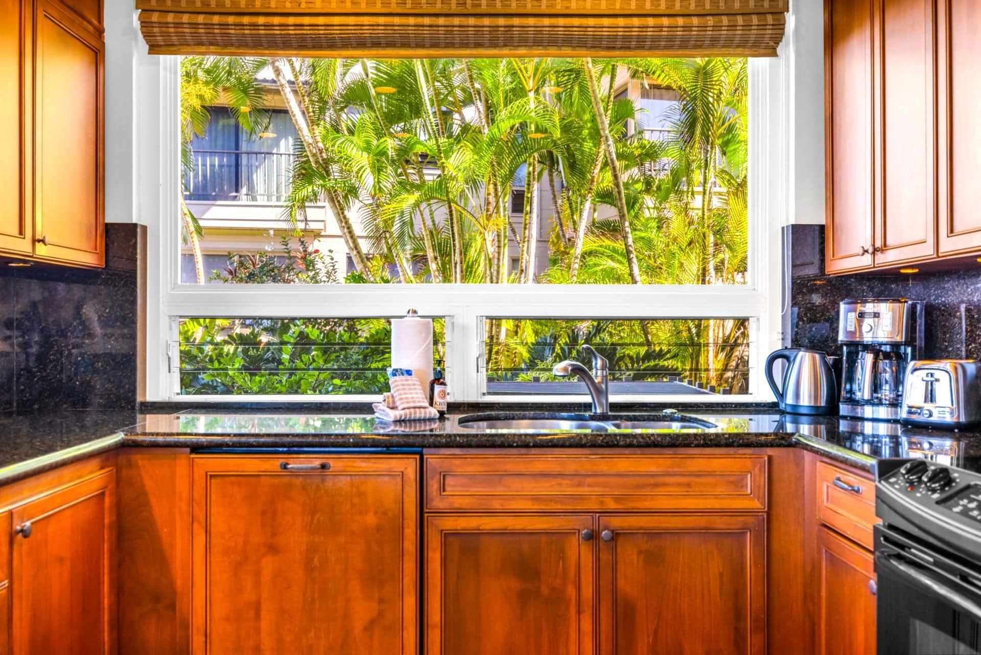 Eine Küche mit Holzausstattung, einem Edelstahlspülbecken und einem Fenster mit Blick auf einen tropischen Garten.