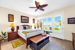 A bedroom with a bed, bedside lamps, a ceiling fan, a window with blinds, and artwork on the walls.