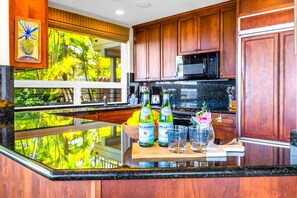 A kitchen with wooden cabinets, a black microwave, and a large window with a view of greenery.