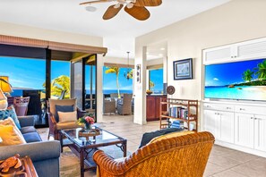 A spacious living room with a large TV, comfortable seating, and a view of the ocean.