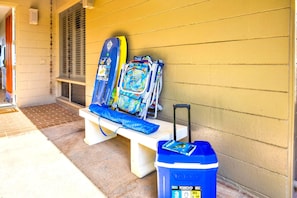 A bench with a suitcase and a trash bin outside a building.