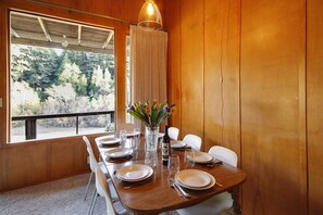A dining table set with plates, glasses, and a bottle, with a vase of flowers in the center. - Riverview ~ Riverfront MCM Gem. A favorite for Family Holidays! Woof (Guerneville)