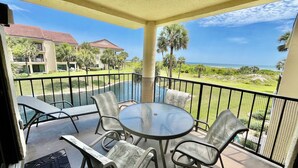 Varanda com mesa e cadeiras de vidro, com vista para uma piscina e o oceano.