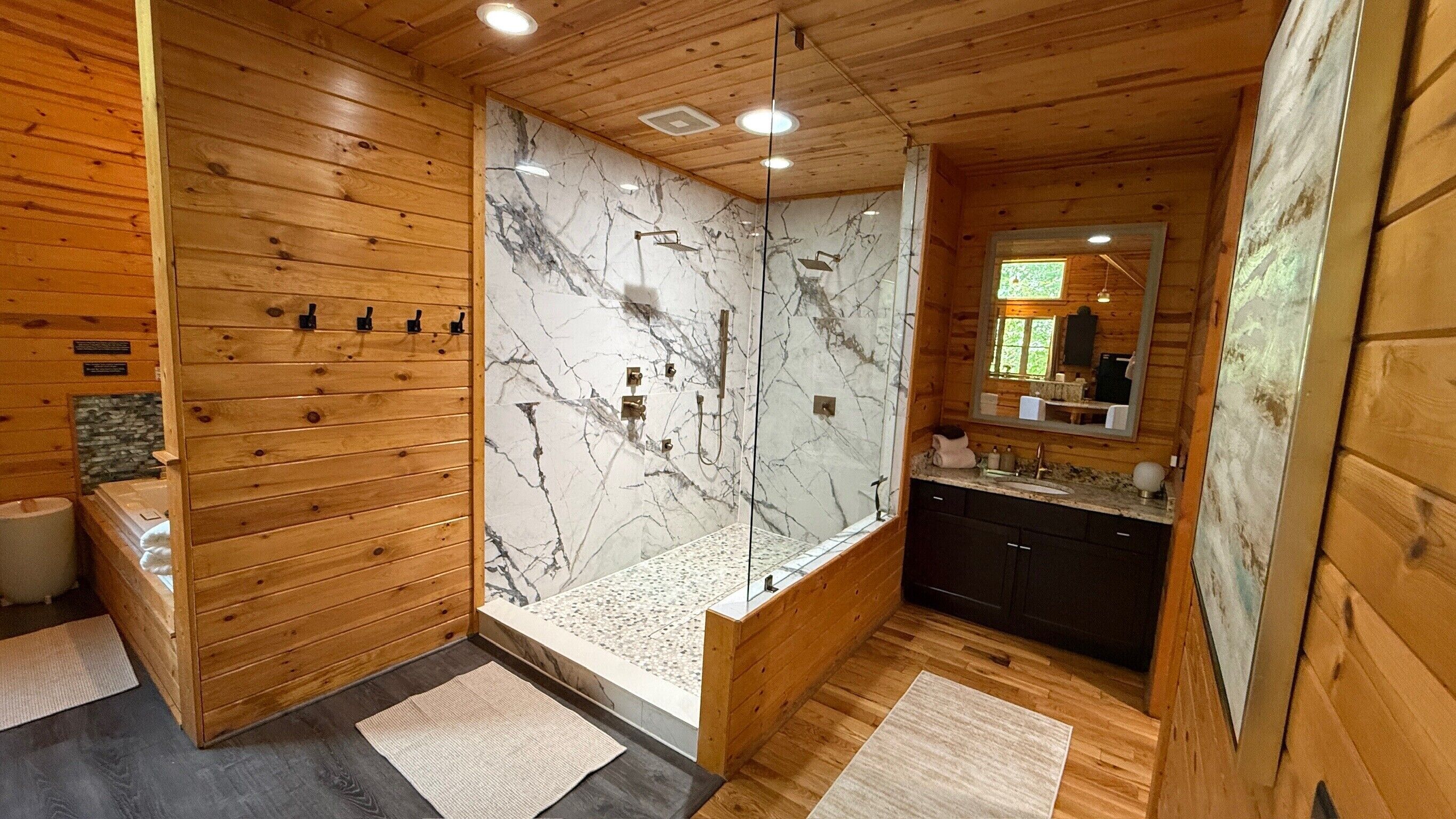 Baño de cabaña de madera con pared de ducha de mármol, armarios de madera y un espejo grande.