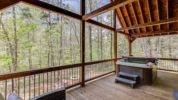 Une terrasse en bois avec un jacuzzi, des bancs et une vue sur une forêt.