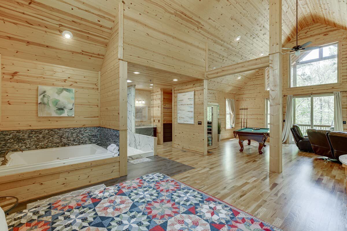 Una cabaña de madera espaciosa con una bañera grande, mesa de billar y alfombra acolchada.
